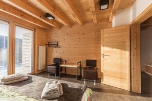 A wooden-paneled room with a bed, two chairs, a table, and a radiator.