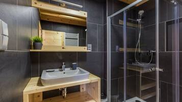 Un baño moderno con tocador de madera, un lavamanos, un espejo y una ducha con mampara de vidrio.