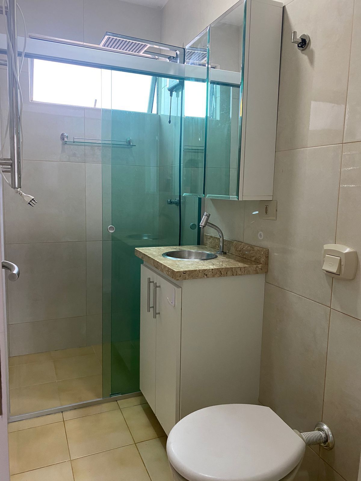 A bathroom with a glass-enclosed shower, a sink with a marble countertop, a toilet, and a mirror above the sink.
