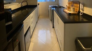 Een moderne keuken met witte kasten, een zwart aanrecht en een uitzicht op de stad door een groot raam.