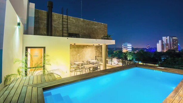 Un edificio moderno con piscina en la azotea, mobiliario exterior y vista del horizonte de la ciudad de noche.