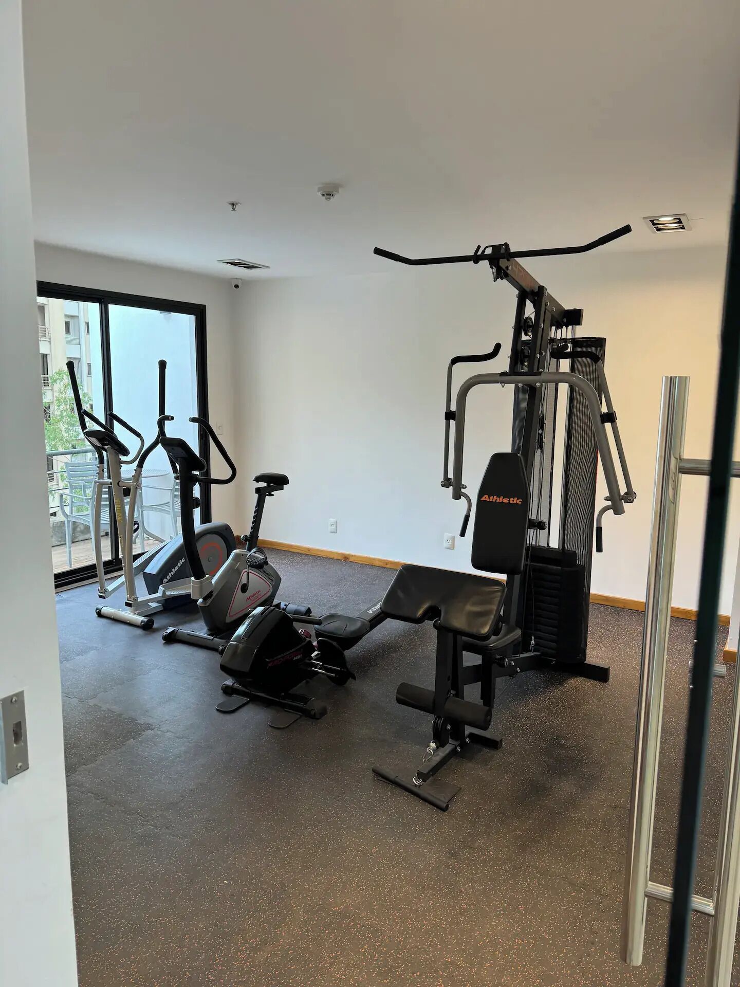Ein Fitnessstudio mit unterschiedlichen Trainingsgeräten, darunter Laufbänder und Kraftgeräte, mit großen Fenstern und einer schlichten weißen Wand.