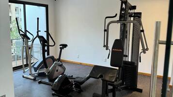 Ein Fitnessstudio mit unterschiedlichen Trainingsgeräten, darunter Laufbänder und Kraftgeräte, mit großen Fenstern und einer schlichten weißen Wand.