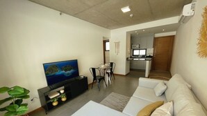Una sala de estar moderna con televisor de pantalla plana, un sofá, un comedor y una cocina al fondo.