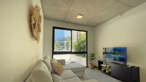 Una sala de estar moderna con un ventanal grande, un televisor de pantalla plana, un sofá y un elemento decorativo en la pared.