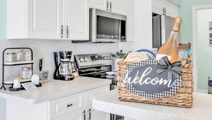 Une cuisine avec des meubles blancs, un four à micro-ondes, une machine à café et un panier en osier orné d’une pancarte « Bienvenue ».