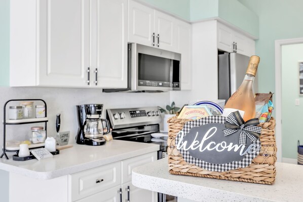 Cocina con armarios blancos, microondas, cafetera y una cesta de mimbre con un cartel que dice 'bienvenido'.