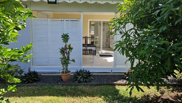 Une petite maison à l’extérieur blanc, dotée d’une porte-fenêtre coulissante et d’une plante en pot placée au premier plan.