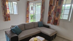 Un salon avec un canapé d’angle, une petite table ronde ornée d’une bougie et un tapis à motifs.