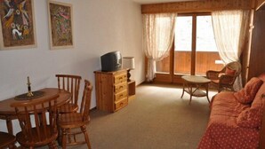 Une pièce chaleureuse avec une table à manger en bois, des chaises, un canapé, un téléviseur posé sur un meuble en bois, et deux œuvres d’art encadrées accrochées au mur.