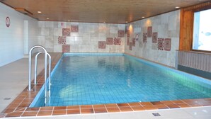 Une piscine intérieure avec un sol et des murs carrelés, un plafond en bois et un escalier en métal.