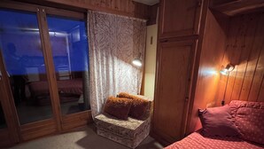 Une chambre confortable au décor intérieur en bois, avec une porte-fenêtre coulissante donnant sur un balcon et un petit coin salon agrémenté de coussins.