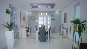 A modern hotel lobby with a reception desk, a dining area with a table and chairs, and decorative plants. - Distribución (mayaguez)