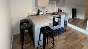 Een compacte keuken met een centraal eiland, barstoelen, een gasfornuis en een hangende lamp.