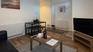 Een woonkamer met een zwarte leren bank, een houten salontafel, een televisie en een schilderij aan de muur.