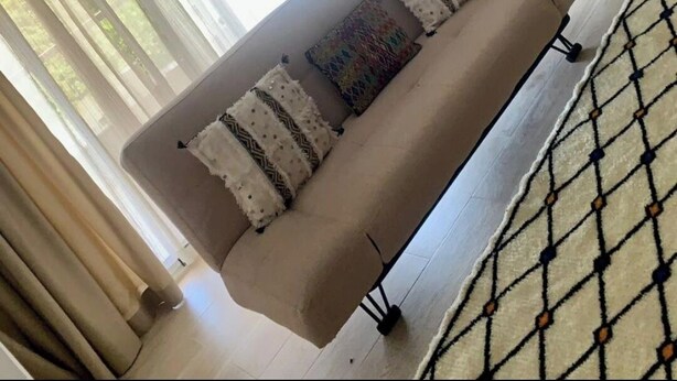 Ein Wohnzimmer mit einem beigefarbenen Sofa, gemusterten Kissen und einem Teppich mit Muster.