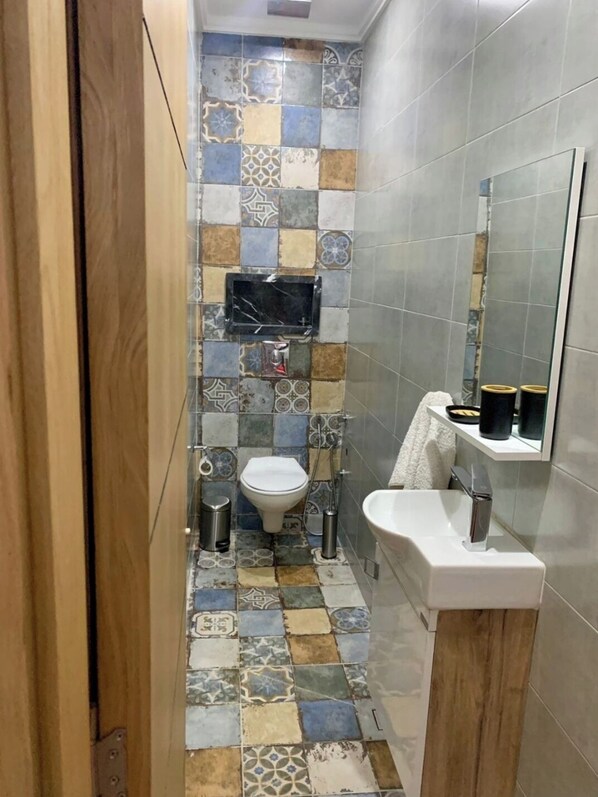 Une salle de bain avec un sol carrelé, des toilettes, un lavabo et un miroir.