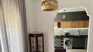 Ein Essbereich mit einem Holztisch, Stühlen und einer Glasvase. Durch einen Bogen ist eine Küche mit modernen Geräten erkennbar.