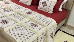 Ein ordentlich bezogenes Bett mit roter und weißer Bettwäsche, einer rot-weißen Kissenauflage und einem Teppich mit geometrischen Mustern.