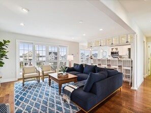 A spacious living room with a sectional sofa, a dining area with a white table, and a kitchen with white cabinets.