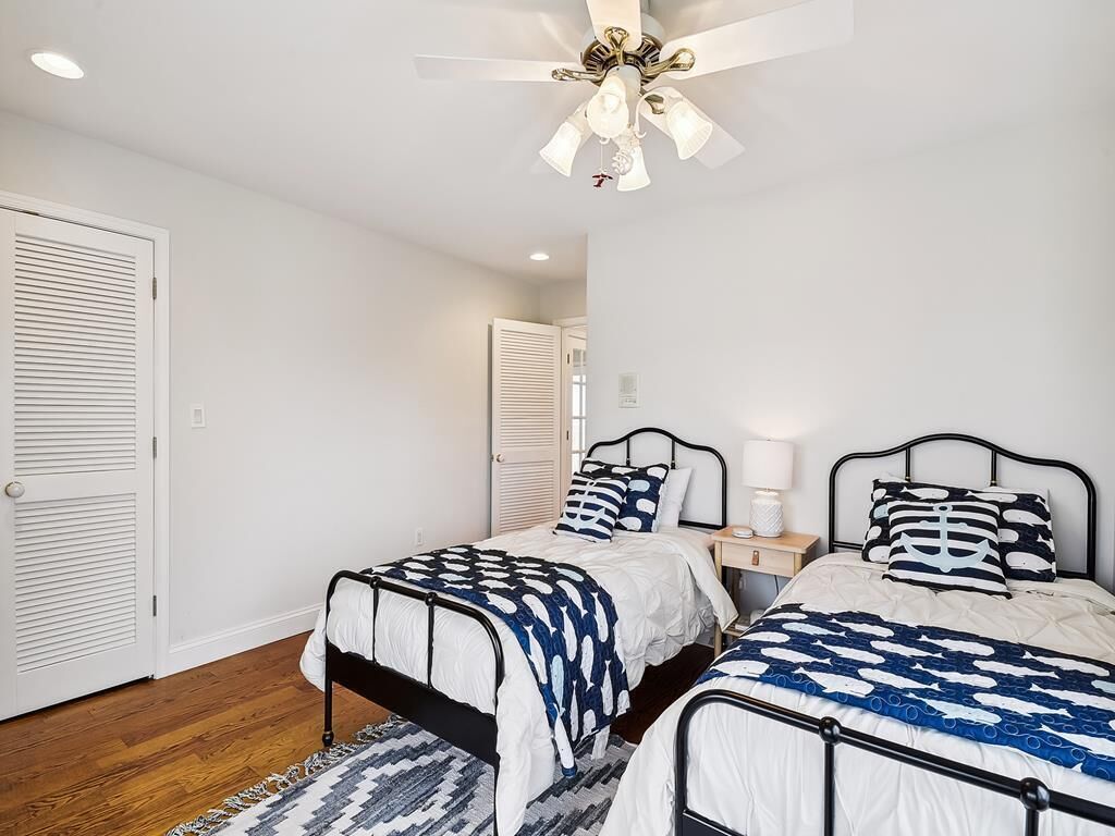 A bedroom with two beds, a ceiling fan, bedside tables, and a wooden floor.