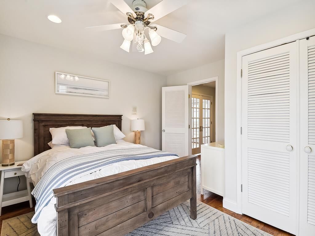 A bedroom with a wooden bed, white walls, a ceiling fan, and a white door with louvered panels.