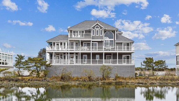 Une grande maison à deux étages, dotée d’un balcon, d’une grande fenêtre et dont le reflet se mire dans l’eau.