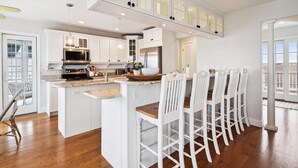 Une cuisine avec des meubles blancs, un îlot central et un coin repas avec des chaises blanches.