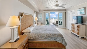 Ein Schlafzimmer mit Bett, Nachttischlampen, einem Fernseher, einem Deckenventilator und Meerblick.