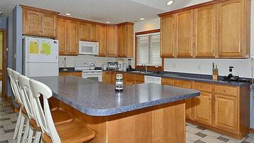 A kitchen with wooden cabinets, a granite countertop, a refrigerator, a microwave, and a sink.
