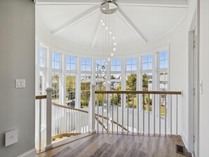 Una habitación con techo abovedado, ventanas amplias, escalera de madera y vistas al exterior.