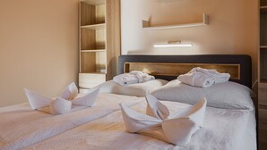Ein Hotelzimmer mit zwei Betten, jedes mit Handtüchern, die zu Schwänen geformt sind, einem Holzschrank und einer Ablage mit einem 'LOVE'-Schild.