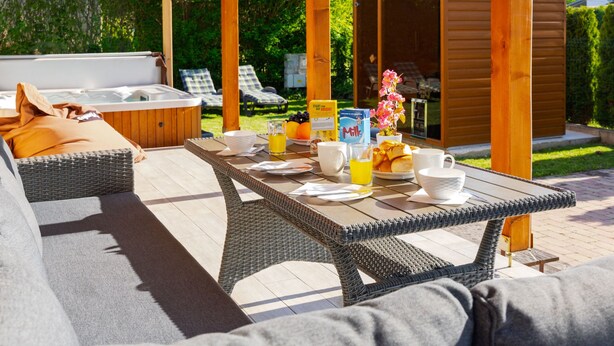 Ein überdachter Außenbereich mit Whirlpool, Liegestühlen und einem Frühstückstisch.