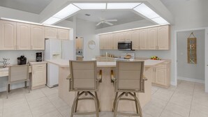 Een moderne keuken met een centraal eiland, lichte houten keukenkastjes en een plafondventilator.