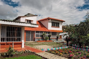 Un edificio de dos pisos con techo de tejas rojas, ventanas grandes y un jardín con flores coloridas.