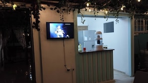 Une pièce avec un téléviseur fixé au mur, un petit comptoir avec une machine à café et une porte donnant sur une autre pièce.