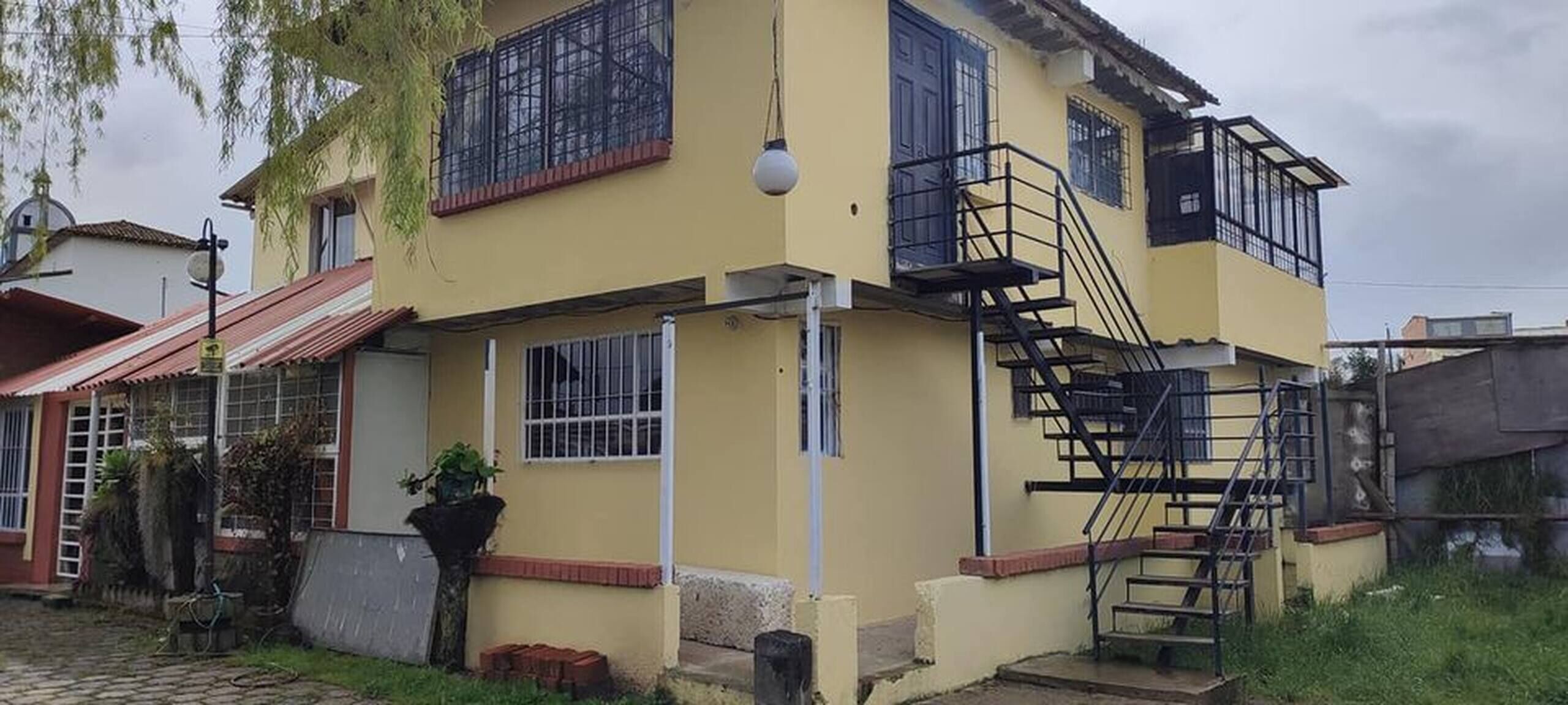 Un edificio de dos pisos con fachada amarilla, una escalera negra y ventanas con barrotes.