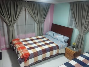 Un dormitorio con cama, cortinas, una mesita de noche y una pequeña mesa con una planta.