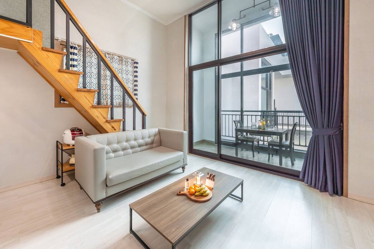 Una sala moderna con sofá, mesa de centro y escalera con cortinas estampadas.