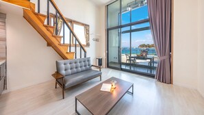 Un salon moderne avec un canapé gris, une table basse en bois et un escalier menant à l’étage supérieur.