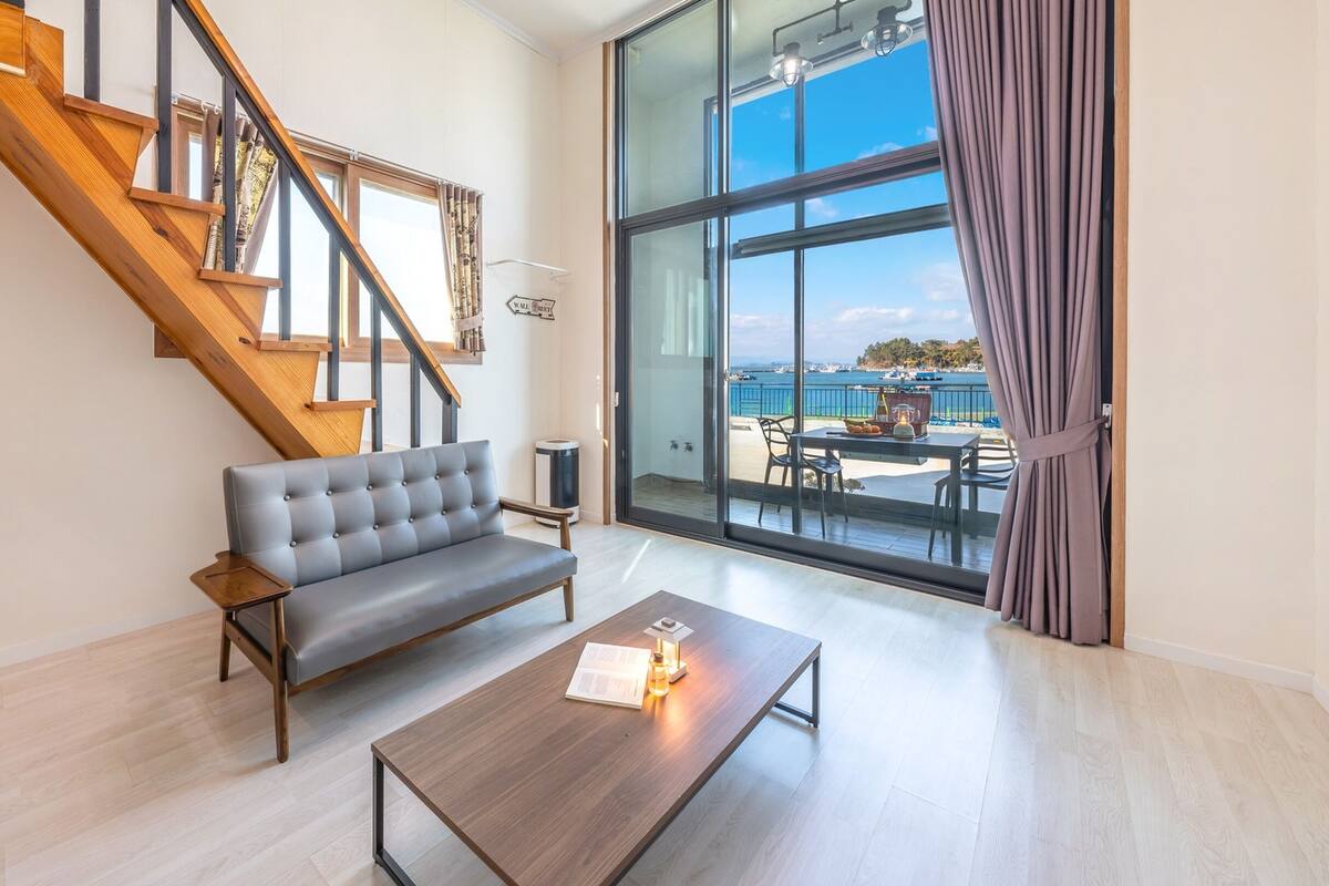 Una sala de estar moderna con un sofá gris, una mesa de centro de madera y una escalera que sube a un piso superior.