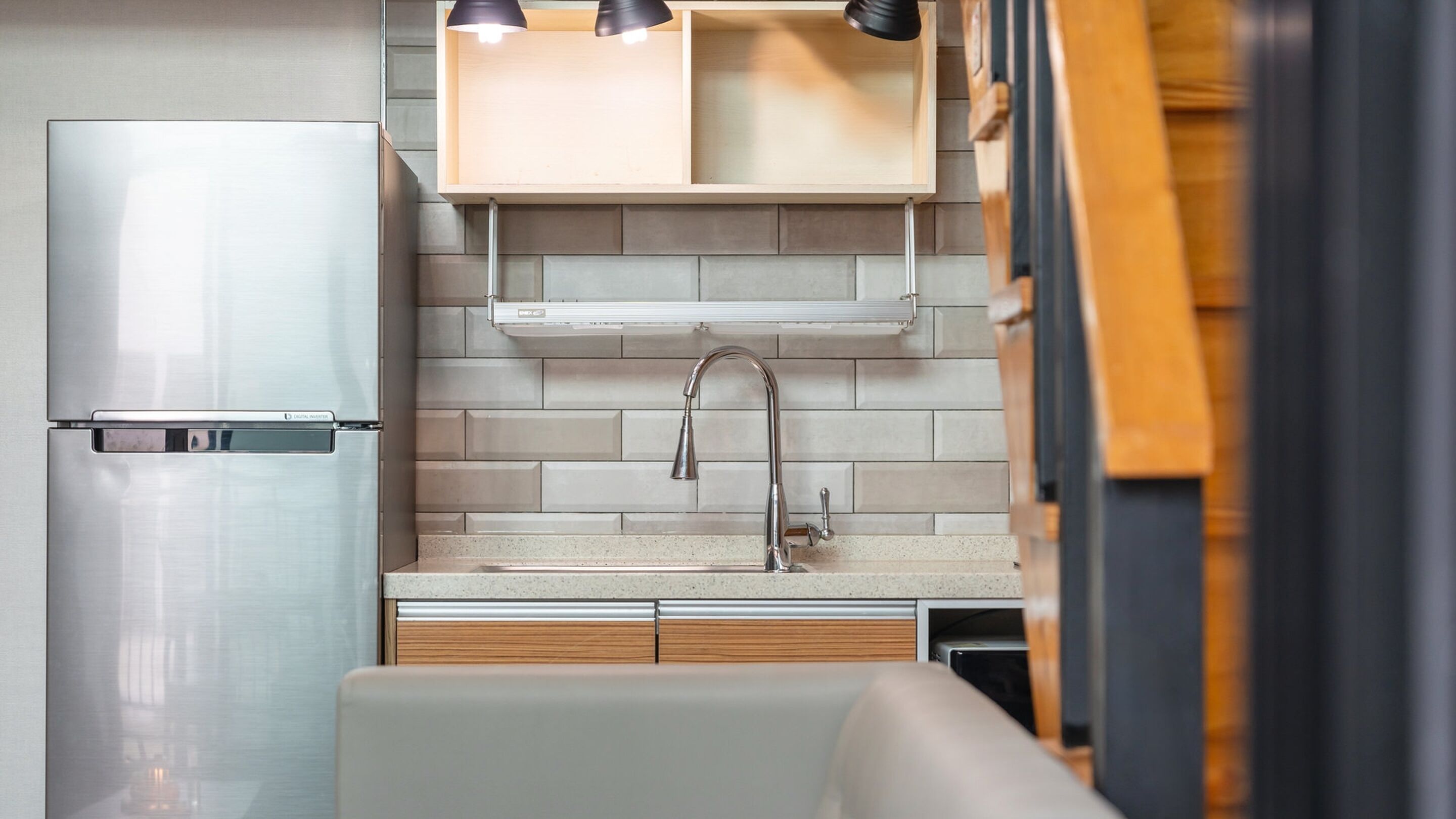 Cocina compacta con refrigerador de acero inoxidable, un lavamanos con grifo moderno y armarios de madera sobre la encimera.