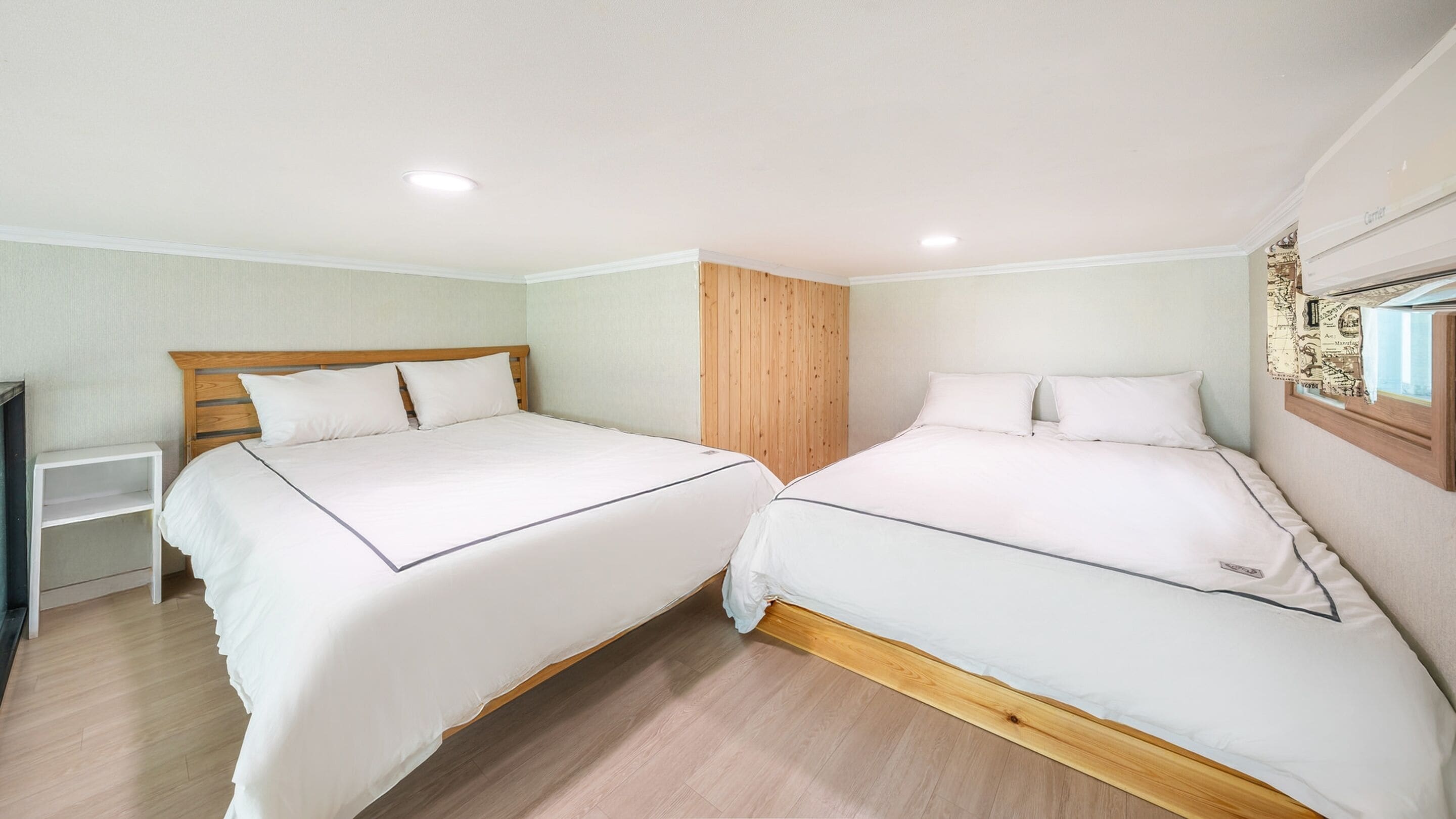 A hotel room with two beds, a wooden wardrobe, a small white shelf, and a window with a map decoration.