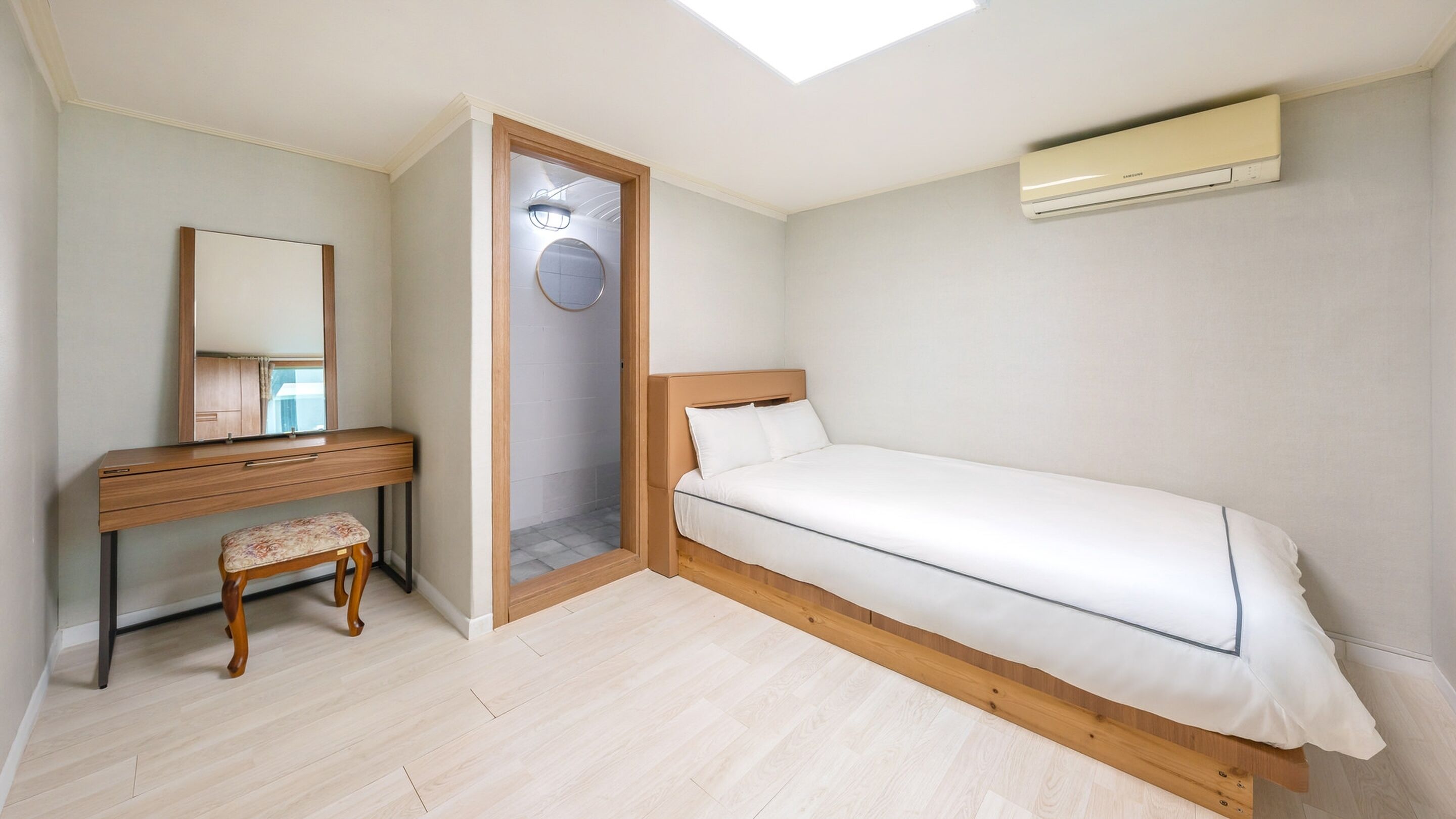 A bedroom with a bed, a desk with a chair, a mirror, and an air conditioning unit.