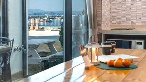 Une cuisine moderne donnant sur un port, une table à manger ornée d’oranges et un banc en bois à l’extérieur.