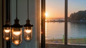 Une vue d’un coucher de soleil sur une étendue d’eau, avec des structures industrielles et une clôture verte au premier plan.