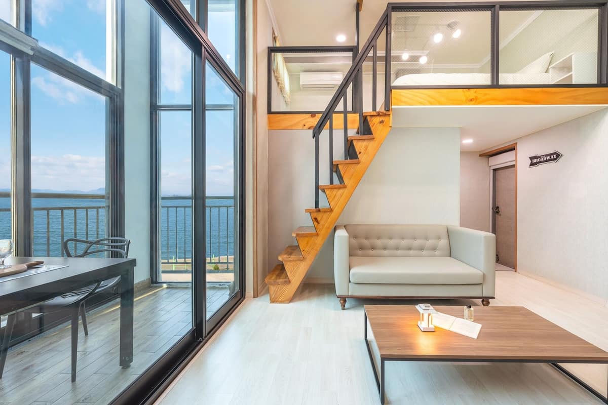 Una sala moderna con vista al mar, una escalera de madera y un sofá.