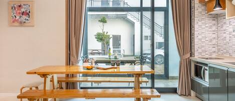 A modern kitchen with a wooden table and benches, a view of the outside, and a dining area with a plant and tableware.