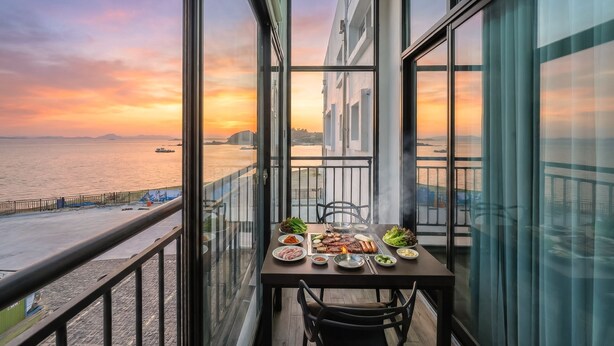 Un balcon avec une table dressée pour un repas, donnant sur le bord de l’eau et offrant une vue sur le coucher de soleil.