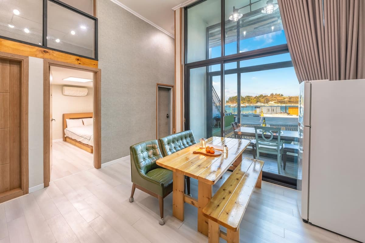 Una cocina moderna con una mesa y banco de madera, ventanas amplias con vista al mar y un techo alto con vigas a la vista.